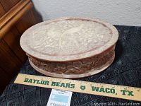 Photo showing the top view of the oval carved box, with detailed floral relief design on lid. A ruler is placed for scale showing about 12 inches width.
