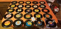 Photo showing 37 vinyl 45 RPM records laid out on a table in rows, showcasing labels and condition of the discs.