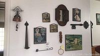 Wide view of all wall art pieces installed on a white wall: includes framed art, a large vintage iron key, small mirror, wooden spoon, candle holder, and other smaller decor items.
