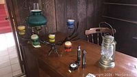 Photo showing metal 5-candle candelabra with multi-colored candle holders, metal kerosene lantern, two metal flashlights, and hanging click light on wood table.