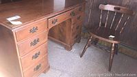 Wood desk with seven drawers and metal handles shown alongside matching wooden chair; visible wear and scratches on surfaces.