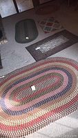 Photo showing six rugs and mats on floor including large oval multicolor braided rug and smaller rugs with geometric patterns