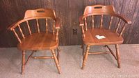 Two wooden captain chairs side by side against a wood-paneled wall, showing overall design and condition.