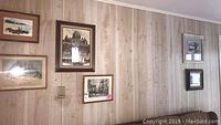 Wall showing 5 framed pieces of art hung on a wood-paneled wall, including various landscapes and architectural images.