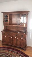 Full view of Ethan Allen wooden china hutch showing upper glass doors with diamond mullions and lower storage cabinets with metal hardware.