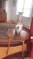 Round wood side table with decorative vase placed on top, set in room with braided rug and wooden floor