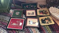12 pcs of framed wall art displayed on braided rug, showing various needlepoint and wood art pieces with floral, duck, and fruit motifs.
