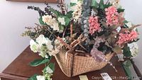Silk flower arrangement in a woven basket with mixed flowers and leaves on wooden surface