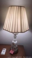 Close-up of a table lamp with a decorative white base and pleated beige lampshade