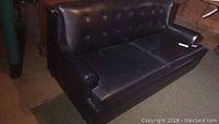 Front view of the black vinyl two-cushion sleeper sofa with button tufted backrest, showing cushion cracks.