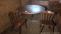 Photo of round wood pedestal table with two wood chairs in basement setting, showing surface wear on table.