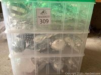 Three clear plastic stackable storage boxes filled with various silver and clear Christmas ornaments.