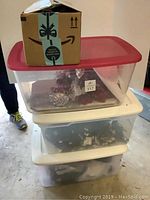 Stack of three containers: a cardboard box on top, and two large plastic totes beneath with Christmas items inside.
