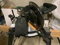 Full view of the Rockwell Shop Series RK7136 miter saw mounted on its integrated stand. The saw has a black blade guard, yellow mechanism, and dust collection bag attached.