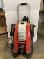 Front view of the red PowerStroke pressure washer showing the unit with handle, hoses coiled on either side, and brand label.