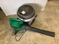 Photo shows Vornado small electric fan next to the green Weed Eater electric leaf blower with power cord coiled.