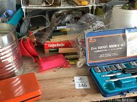 Photo showing 21-piece socket wrench set in blue case, red handled box cutter, and various tools on wooden table