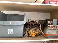 Shelf with Black and Decker 5-inch bench grinder box, assorted ropes, and gray storage bin