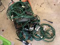 Top view of coiled green extension cords and outdoor timer string lights tangled together on the floor.