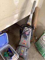 Bissell ProHeat carpet cleaner upright with power cord wrapped, placed on floor next to rolled carpet.