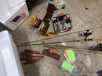 Fishing rods, tackle boxes with lures and flies, knives with sheaths, and styrofoam coolers on concrete floor.