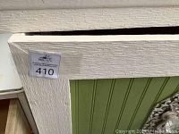 Close-up of corner showing cream textured finish of the cabinet frame and a sticker with lot number.