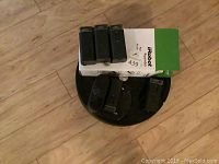 Black iRobot Roomba vacuum cleaner with three battery packs and accessory box on wooden floor.