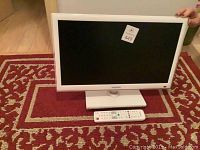 White Samsung flat screen TV on top of red and beige patterned rug with remote placed in front