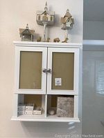 Full front view of white bathroom cabinet with items inside and decor on top