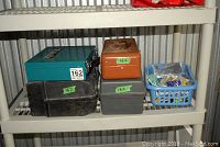 Four metal/tool cases and a small basket with assorted small parts on a plastic shelf