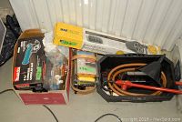 Full view of the lot showing the boxed Makita cordless circular saw, MaxWorks tire rack box on top, Husky black tool caddy holding hand tools, and electric flares to the right.