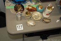 Photo showing assortment of vintage lighters including silver plated Ronson Crown lighters, two can-shaped lighters (Coors Light and Budweiser), pottery pieces, and fur-covered items on a grey table