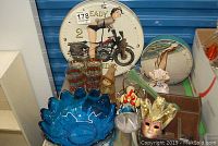 Wide view showing large 14-inch pin-up style quartz clock, four Christmas glasses, blue lotus petal fruit bowl, decorative mask, and small figurines and plates arranged on a table.