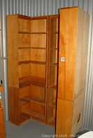 Pair of stacked corner bookshelves photographed in storage unit, showing natural wood finish and angled shelf configuration for corner placement.