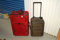 Photo showing the red Delsey and brown Atlantic carry-on suitcases side by side against a metallic panel background.