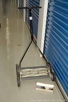 Full view of the McCulloch push reel lawn mower showing the handlebar, wheels, and reel blade assembly. Sharpening kit in box placed beside mower on floor.