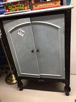 Front view of vintage painted pie safe cabinet with double doors, small round metal knobs, and rounded legs. Paint shows wear and scratches.