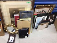 Over 20 assorted framed pieces stacked including prints, embroidery, needlepoint, and mirrors with some gold and black frames.