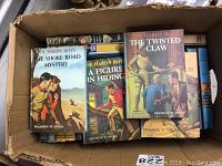 Box containing 26 vintage Hardy Boys books, 13 with original dust jackets, pictured with colorful illustrated covers visible.