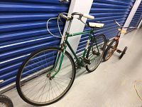 Side angle photo showing the green The Conqueror De Luxe bicycle with white saddle and grips alongside rusty vintage tricycle