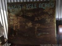 Front view of large antique metal sign showing faded painted text 'Locust Vale Acres' and two Jersey cows, with heavy rust and wear.