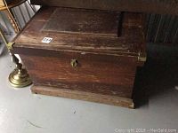 Front view of vintage wood trunk showing brass corner protectors, keyhole, and wood wear.