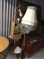 Photo showing the tall wooden table lamp with attached side table, brass lamp with cream shade, glass and ceramic lamps, with some lampshades included and a cardboard box on table