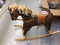 Side profile view showing the brown rocking horse with tan saddle, leather reins, and yarn mane standing on wooden rockers.