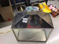 Large square metal and glass candle holder with pyramid-shaped metal top and circular handle on top, shown from the front and above