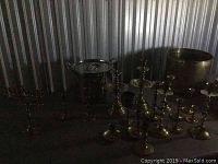 Photo showing multiple brass candle holders and a chrome pot with lid, also includes a large brass planter