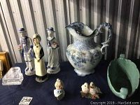 Photo shows Meakin antique pitcher with blue floral pattern, ceramic figurines including a female figurine 9 inches tall, two 13 cm matching figurines, smaller figurines, Abingdon green bowl, and small glass grand piano figurine.
