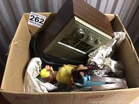 Vintage radio sitting in a cardboard box with two figurines and some hand tools packed around it.