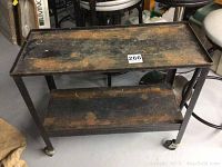 Side view of metal trolley showing rust and wear on two shelves and casters on legs.