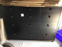 Front view of black wooden dresser with nine drawers and round knobs, showing light wear.